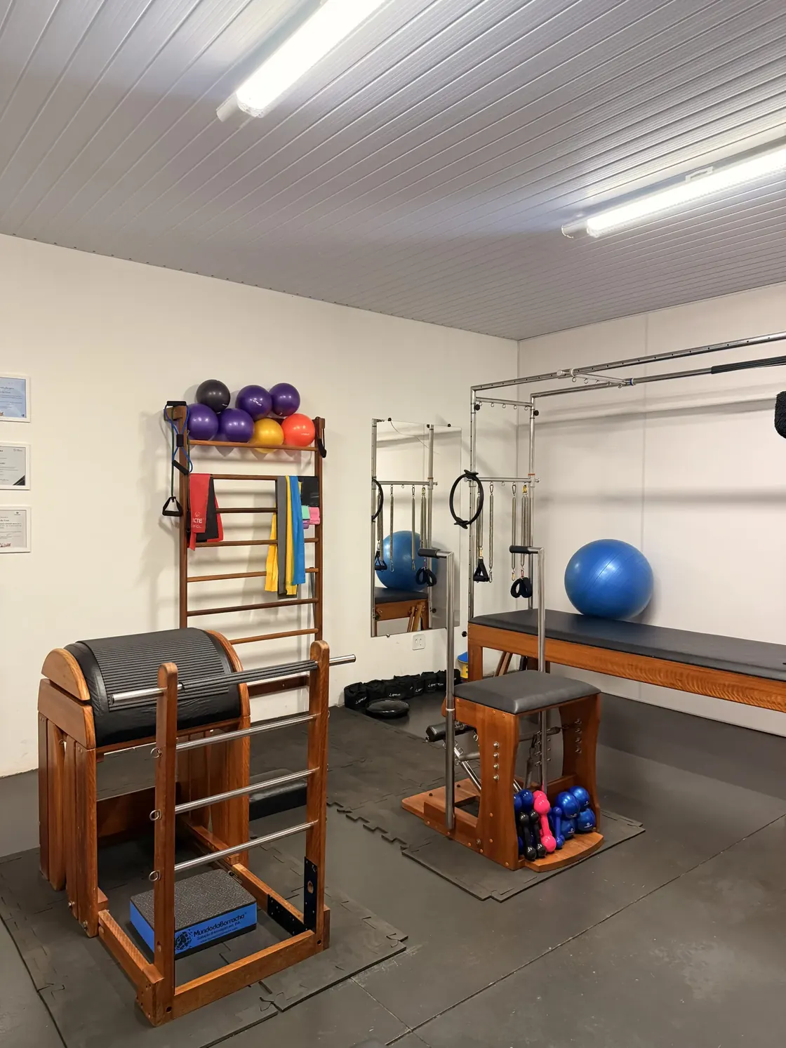 Sala de pilates da Core com barril de madeira, reformer, bolas suíças azuis e roxas, faixas elásticas e halteres organizados na parede