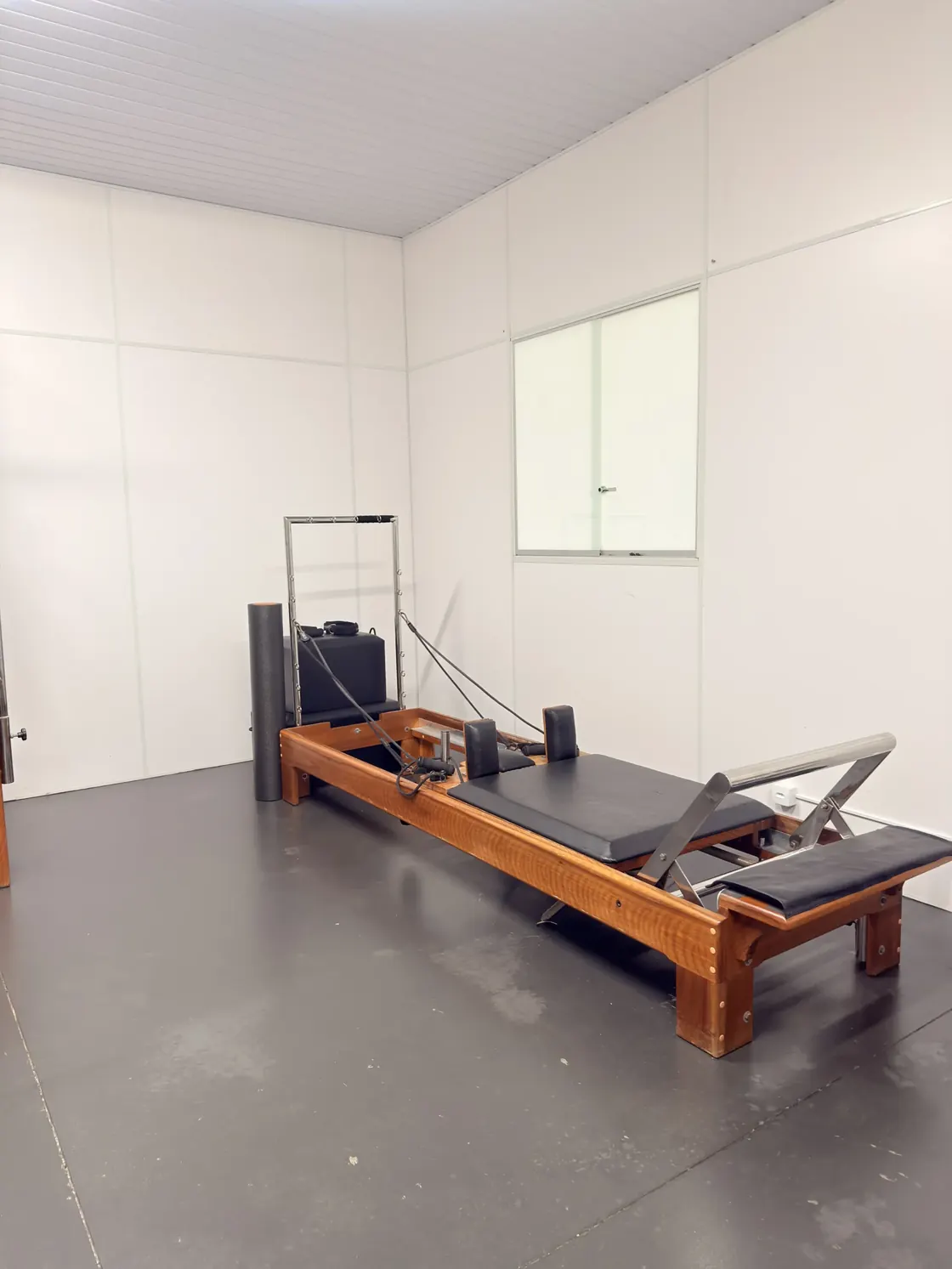 Reformer de pilates em madeira e alumínio numa sala clara da clínica, com espelho na parede ao fundo