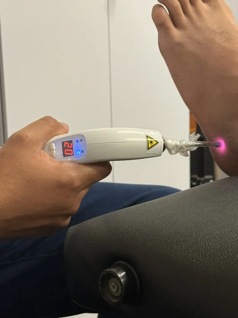 Fisioterapeuta da Core aplicando laser no tornozelo de um paciente; o ponto vermelho do aparelho aparece sobre a pele